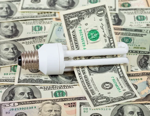 Энергосберегающая лампочка на фоне денег — стоковое фото