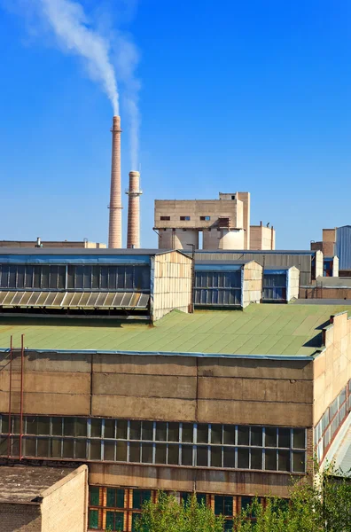 Gran fábrica con chimeneas humeantes contra el cielo azul — Foto de Stock