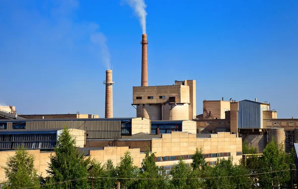 Большая фабрика с дымящимися трубами на фоне голубого неба — стоковое фото