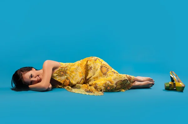 Young woman in yellow lying and laughing on blue background — Stock Photo, Image