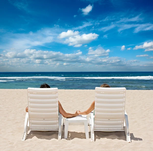 坐在海滩椅子上手牵手靠近大海的情侣 — 图库照片