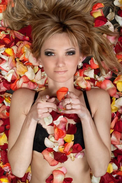 Verspielte junge Blondine liegt in Rosenblättern — Stockfoto