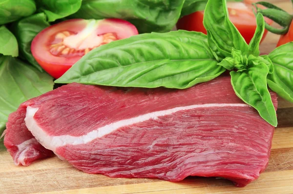 Parte de carne fresca de basílicas e um tomate — Fotografia de Stock