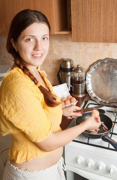 Mulher jovem adiciona ovos à frigideira quente — Fotografia de Stock