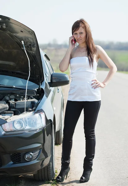 Женщина звонит на мобильный рядом со сломанной машиной — стоковое фото