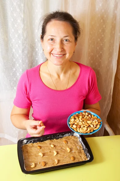 Woman adds nuts into dough — Stock Photo, Image