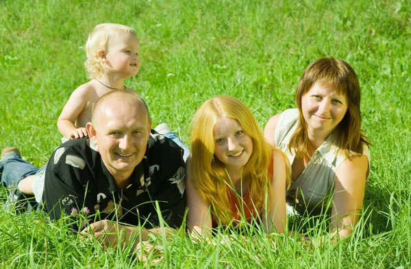 Família de quatro que põem na grama — Fotografia de Stock