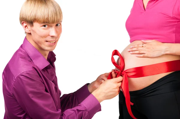 Untying red silk bow on stomach of pregnant woman — Stock Photo, Image