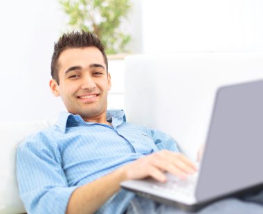 Smiling young man working on laptop computer at home clipart