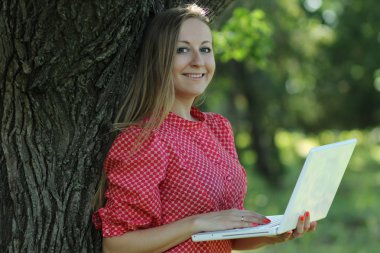 Blond woman having fun with laptop outdoors clipart