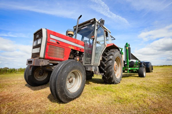 Трактор собирает рулон стога сена в поле — стоковое фото