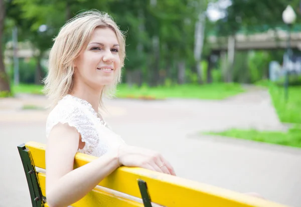 La mujer está sentada en el banco amarillo del parque. —  Fotos de Stock