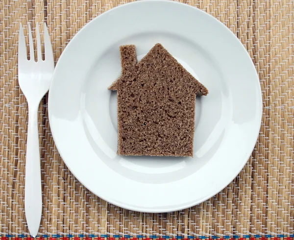Дом, вырезанный из хлеба, лежащий на тарелке . — стоковое фото