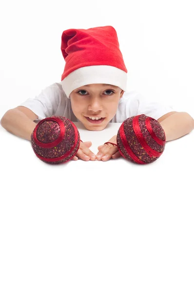 Мальчик в рождественской красной шляпе с красными декоративными шариками — стоковое фото