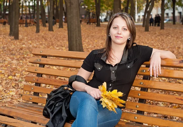 Mooi meisje zittend op een bank in de herfst Park — Stockfoto