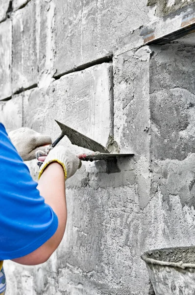 A hand holding a knife applying paint and plaster on a wall.