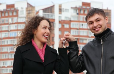 Young couple with key against many-storeyed house clipart