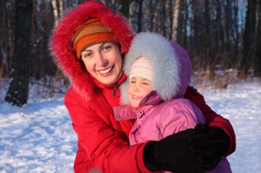 Mother embraces daughter in park in winter clipart