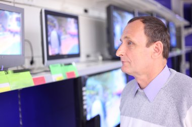 Elderly man in shop looks at TVs clipart