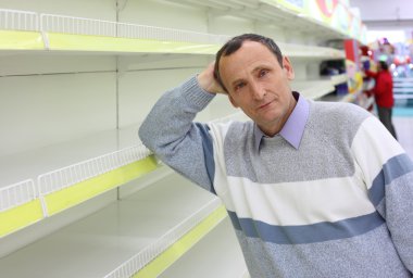 Elderly man leans against empty shelves in shop clipart