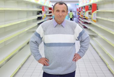 Elderly man stands between empty shelves in shop clipart