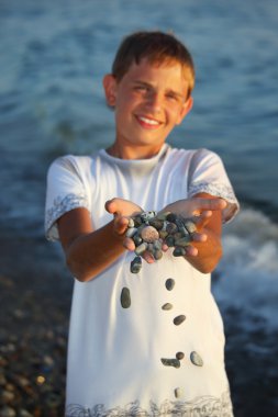 Teenager boy with handful of stones in hands, scatter stones clipart