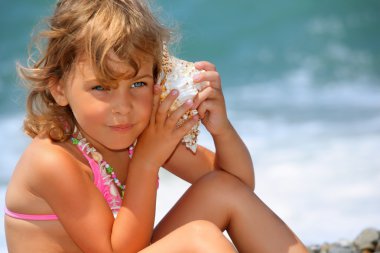 sevimli küçük kız seashell kase sahil üzerinde bir kulak için eğildim
