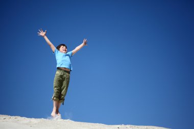 Boy jumps on sand with lifted hands clipart