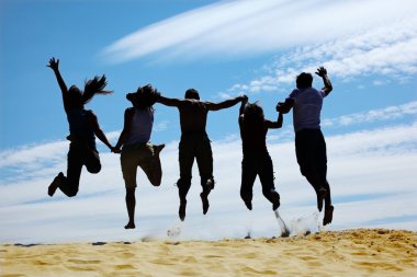 Group of friends jumps on sand, rear view