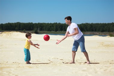 Father and son throw each other ball on sand clipart