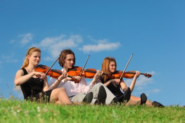 Three violinists sit and play on grass against sky clipart