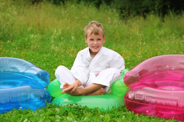 Karate boy sits in inflatable armchair on lawn clipart