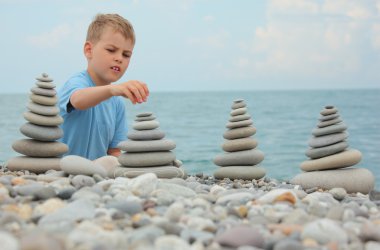 Boy and stone stacks on pebble beach clipart