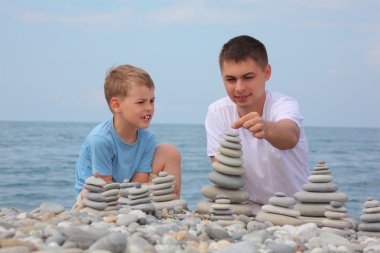 Father and son builds stone stacks on pebble beach clipart