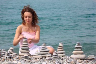 Young woman builds stone stacks on pebble beach clipart