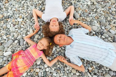 Happy family with little girl lying on stony beach, closed eyes, clipart