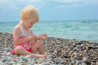 Child sits on pebble beach clipart