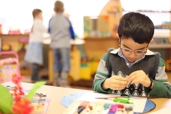 Мальчик в очках из пластилина на столе в детском саду — стоковое фото