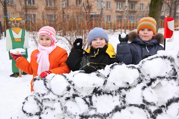 Трое детей на стене снежной крепости во дворе бросают sn — стоковое фото