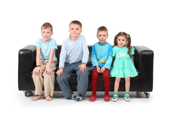 Four children sitting on black leather sofa — Stock Photo, Image