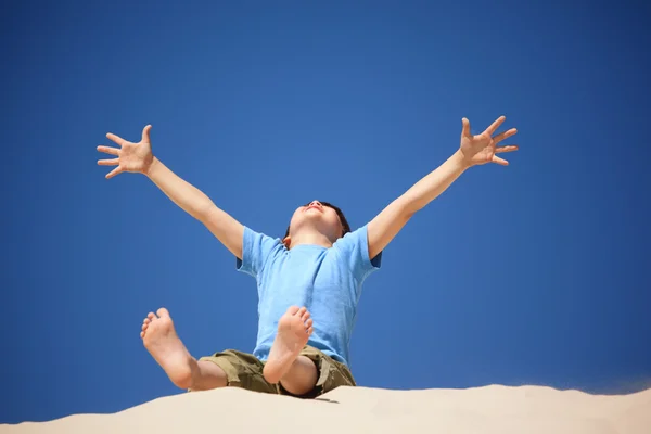 Jongen speelt op het strand, de handen en de benen omhoog — Stockfoto