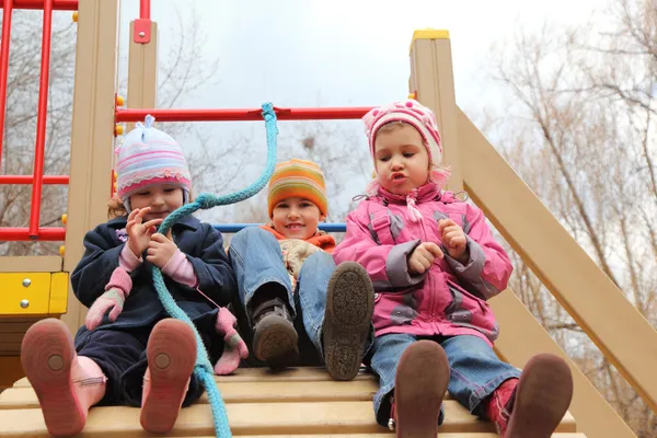 Три дитини сидять на штучному пагорбі на дитячому майданчику — стокове фото