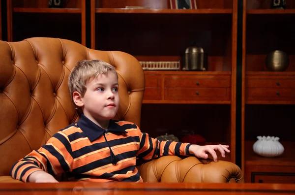 Мальчик сидит в кожаном кресле в роскошном офисе — стоковое фото