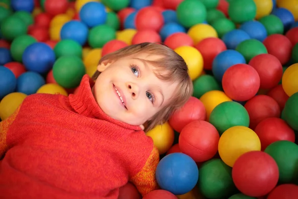Маленькая девочка лежит на разноцветных пластиковых сферах — стоковое фото