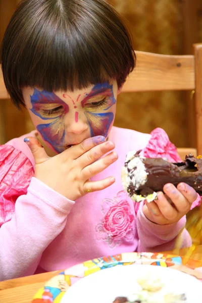 Little girl painted for holiday eats cake — Stock Photo, Image