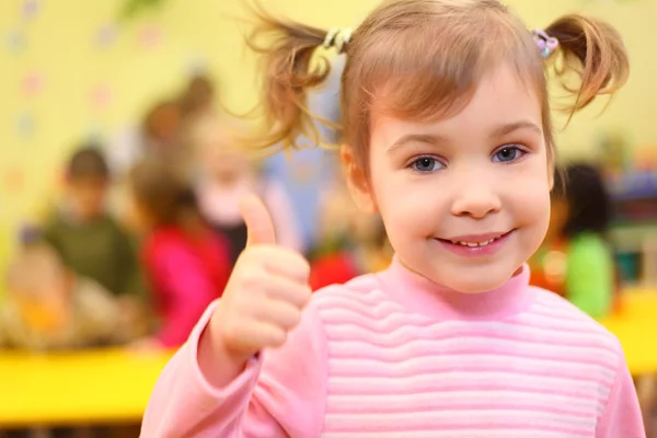 Trochę uśmiechający się dziewczyna w przedszkolu pokazuje znak ok — Zdjęcie stockowe