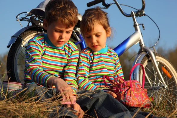 Two children sit on dry grass at bicycle — Stock Photo, Image