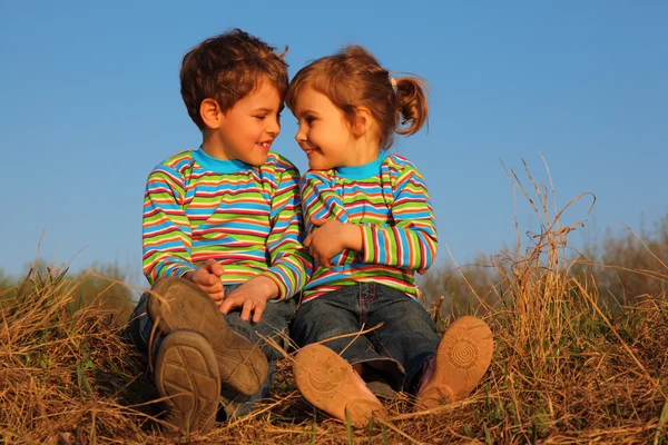 Dwoje dzieci w pasiaste koszulki siedzieć na suchej trawy — Zdjęcie stockowe