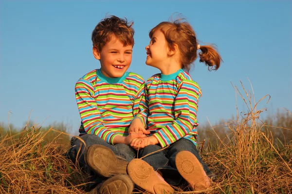 Duas crianças felizes em camisetas listradas sentam-se na grama seca — Fotografia de Stock