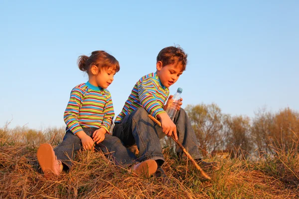 Девочка и мальчик с бутылкой и палкой в полосатых футболках — стоковое фото